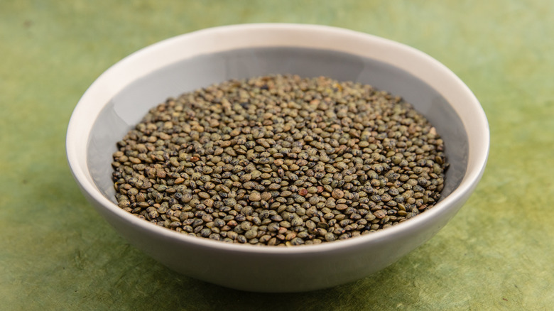 A bowl filled with dried, green lentils.