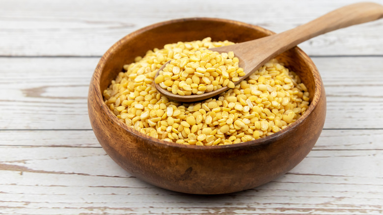 A wooden bowl full of yellow lentils.