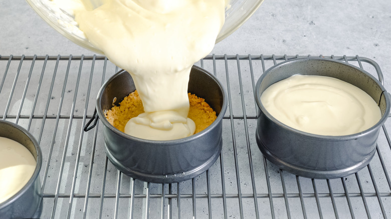 A baker pouring cheesecake batter into individual containers