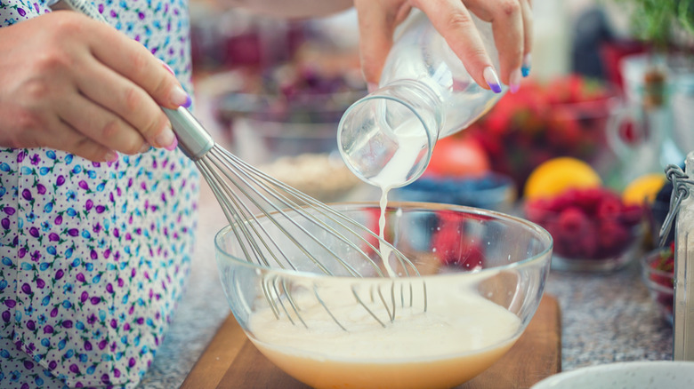 A person adding milk to pancake batter while mixing it with a whisk