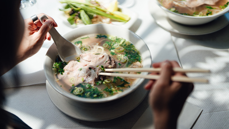 a person eating a bowl of Vietnamese pho