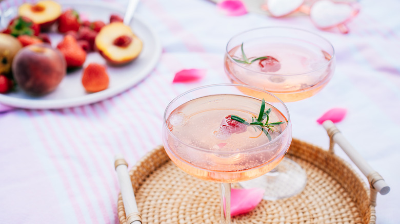 Two coupes on a wicker tray filled with a Prosecco and peach drink.