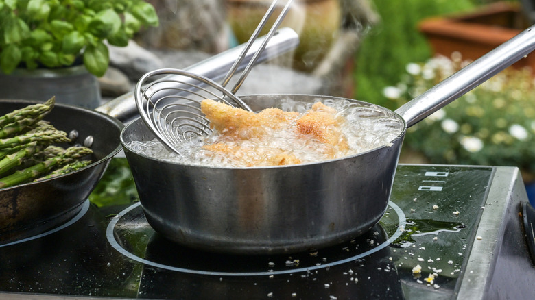 Chicken deep frying on black stove top oven.