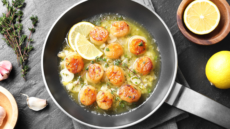 Scallops and lemons frying inside an oily black pan.