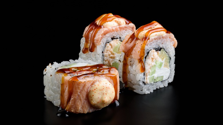 Three pieces of a baked salmon roll on black background