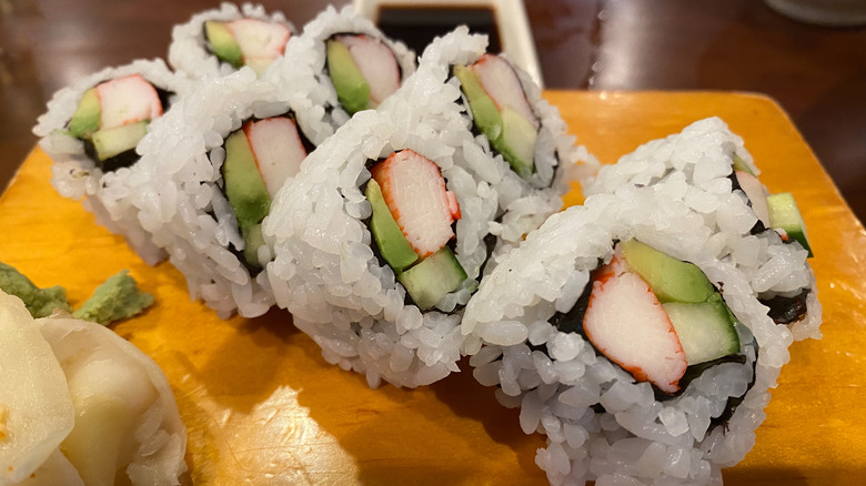 Eight pieces of cut California roll on a wooden board, served with wasabi, ginger and soy sauce