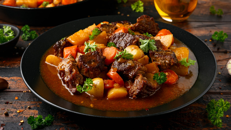 A bowl of beef stew with baby carrots and potatoes sitting on a table.