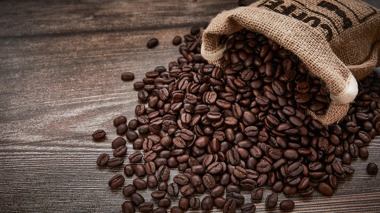 Coffee beans spilling from a burlap bag onto a wooden surface.