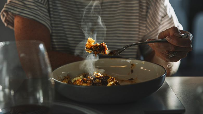 A woman eating from a hot plate of Spaghetti Bolognese.