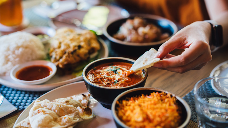 A woman dipping naan in butter chicken while eating Indian food.