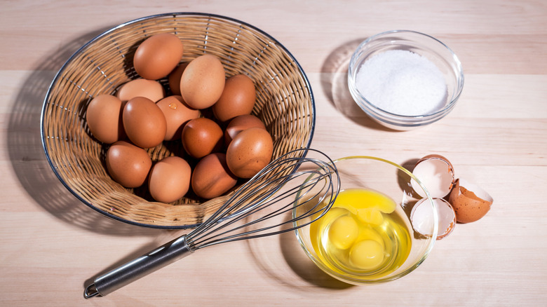 A bowl of chicken eggs with some already cracked in a bowl near sugar