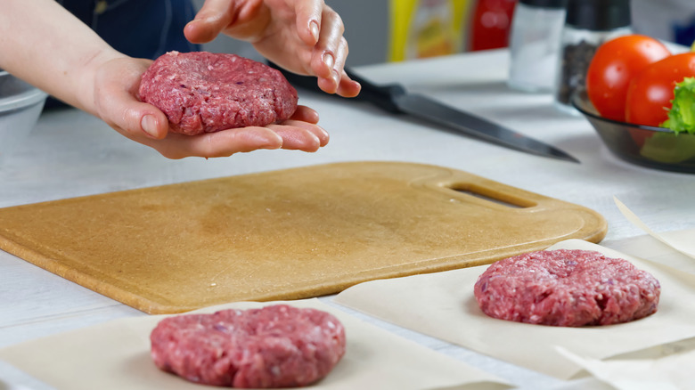 Someone hand smashing hamburger patties on a cutting board