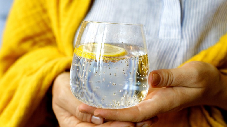 Woman in yellow sweater holds a glass of bubbly water with a slice of lemon