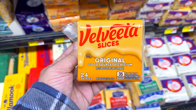 A hand holds a package of Velveeta slices