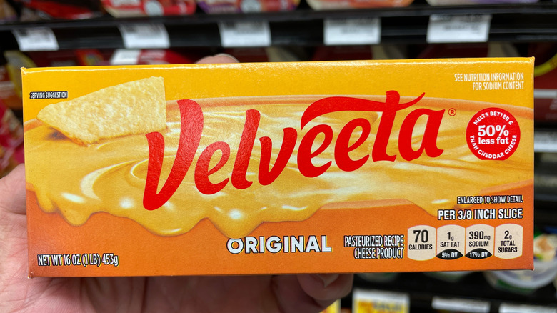 A hand holds a box of velveeta