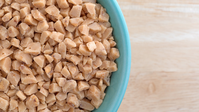 Green bowl of toffee bits on a wooden surface