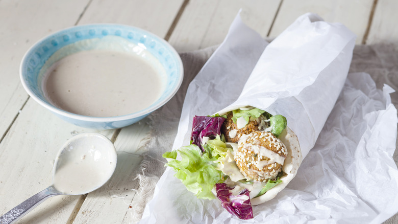 bowl of tahini sauce next to a pita sandwich