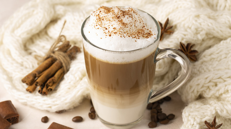 Glass mug of mocha coffee with cinnamon sprinkled on the foam with a cozy cream blanket as the background.