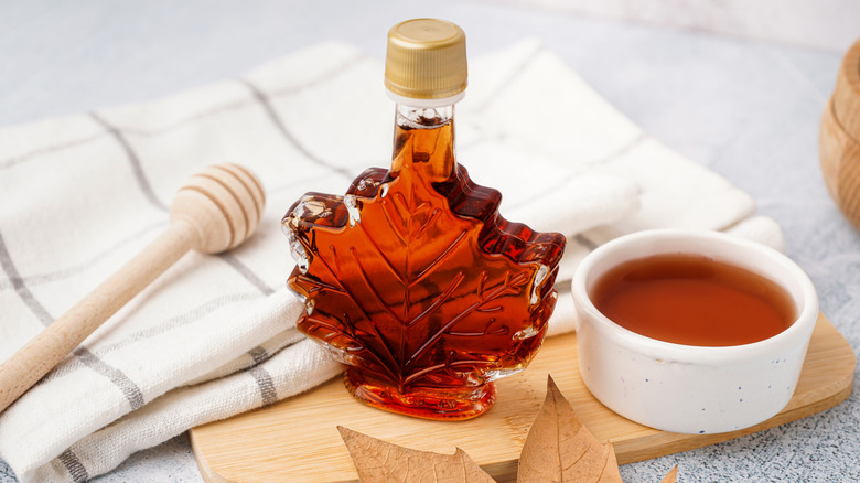 A leaf-shaped bottle of maple syrup beside a dish of maple syrup and a honeycomb wand