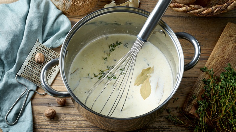 a pot of milk with herbs and a whisk in it