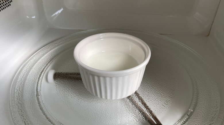 a white ramekin of milk in a microwave