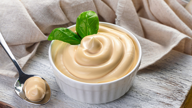 Basil on top of mayo in a ceramic bowl with a spoonful of mayo on the side