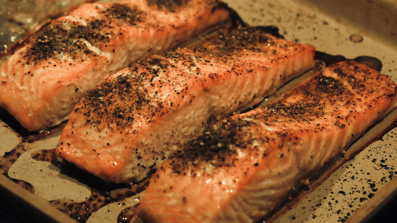 Three salmon filets on a tray sprinkled with black pepper