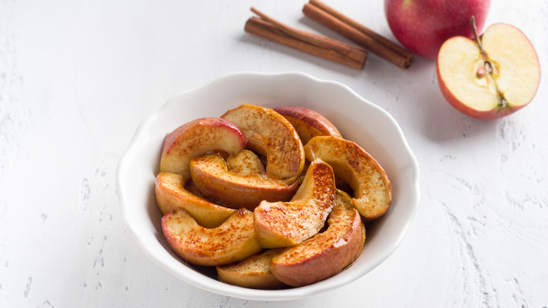 A Bowl full of sliced baked apples with half of an unbaked apple laying beside it