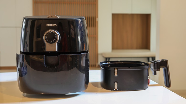 Black air fryer and basket on white table