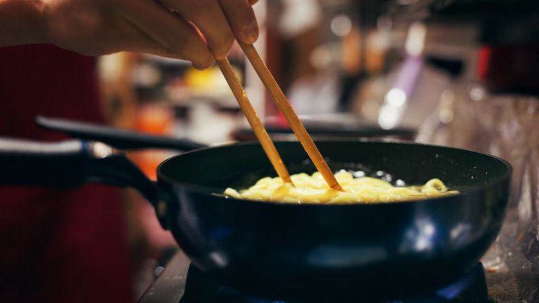 A person stirring noodles with wooden chopsticks.