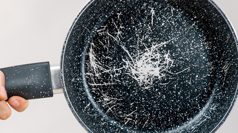 A person holding a non-stick pan covered in scratches