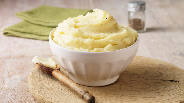 A small bowl of mashed potatoes on a wooden board