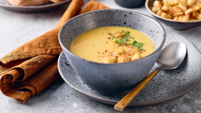 Bowl of mashed potato soup on a plate with a metal spoon nearby