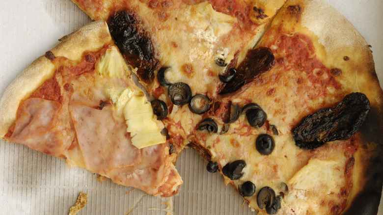 Cold pizza, one slice Hawaiian and two slices cheese with black olives on a cardboard surface stained with oil.