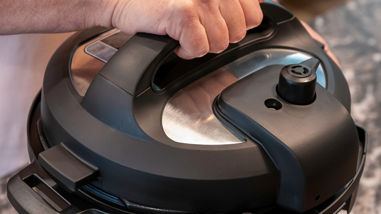 A person grips the handle of an Instant Pot lid