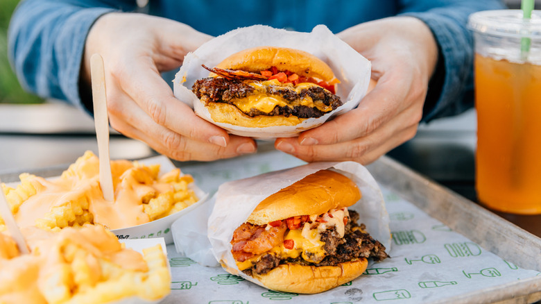 Hands holding a Shake Shack burger.