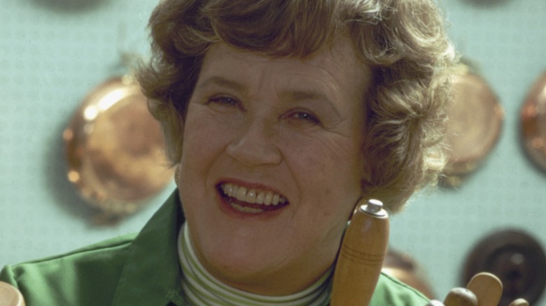 Julia Child posing in her kitchen with various kitchen implements