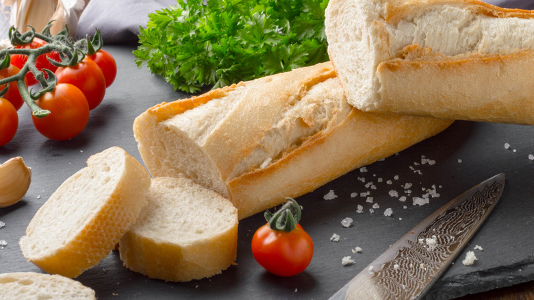 sliced baguette on a black slate board with parsley and cherry tomatoes