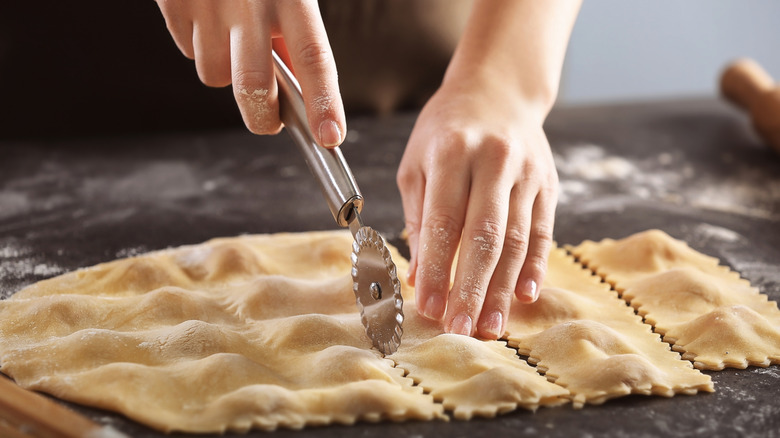 A person cutting ravioli dough using a ravioli cutter.