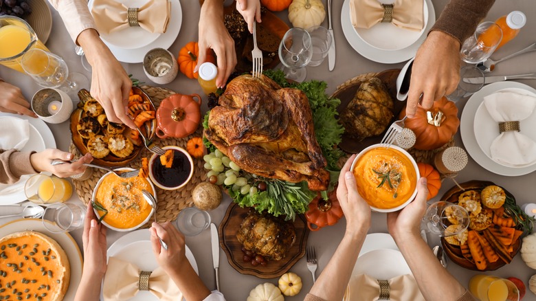 Hands reaching for traditional Thanksgiving foods on a table