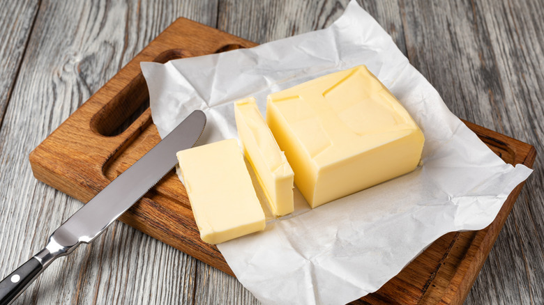 A block of butter in an open wrapper on a wooden chopping board