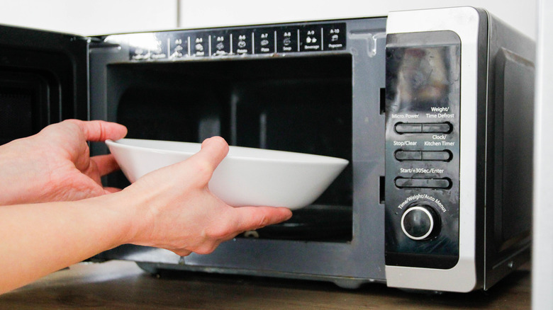 A person putting a white bowl into the microwave