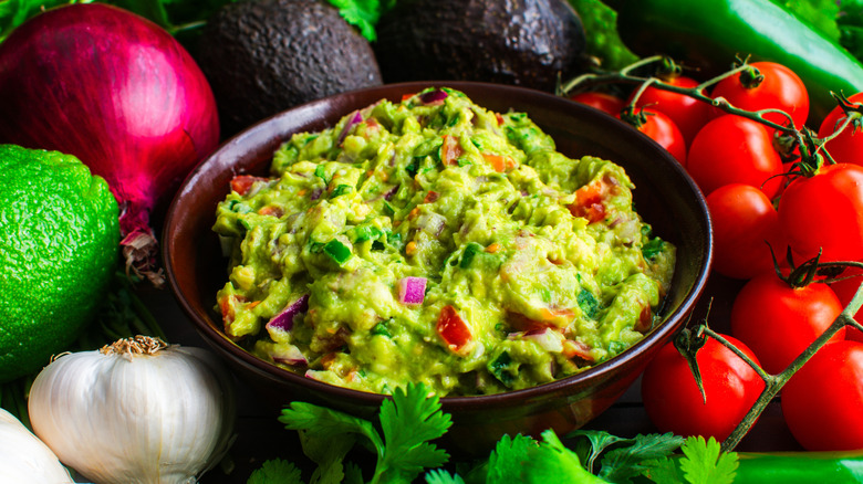 A bowl of avocado guacamole dip with red onion and tomatoes