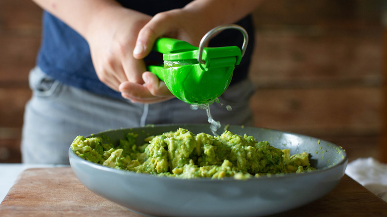 A person squeezing citrus juice into avocado guacamole using a green citrus press