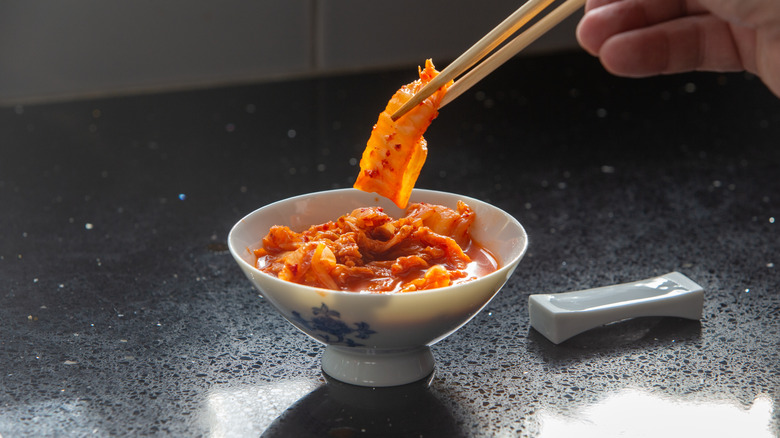 A person eating kimchi from a small bowl with chopsticks