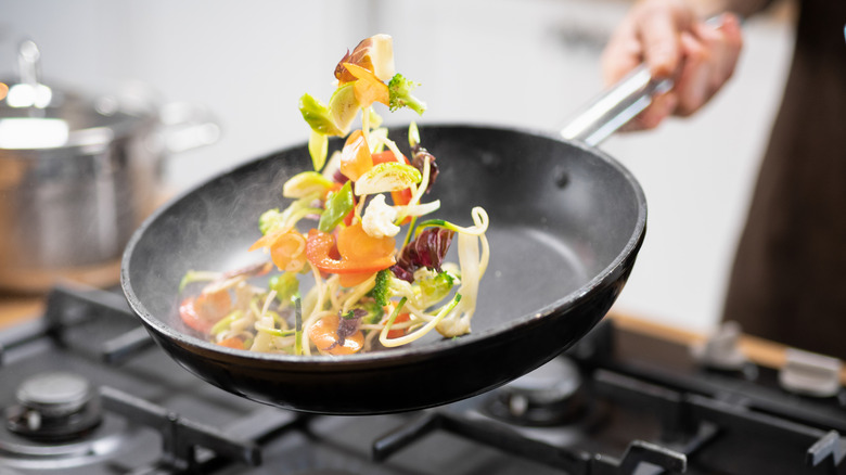 A cook tossing vegetables in a skillet over the stove