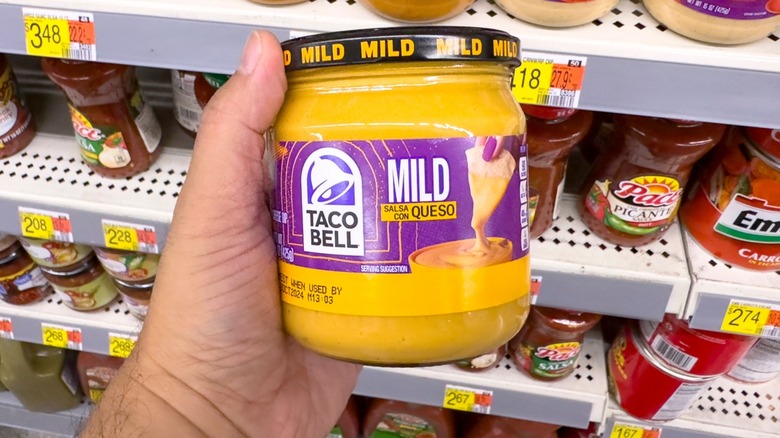 Hand holding Taco Bell mild queso jar