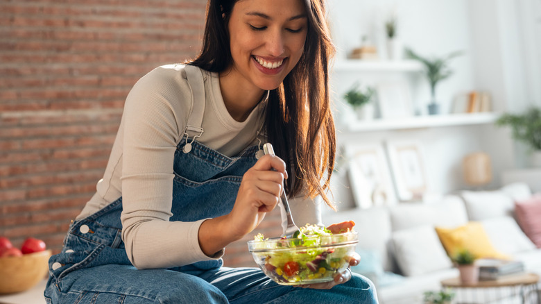 Woman enjoying a salad while sitting on her kitchen counter