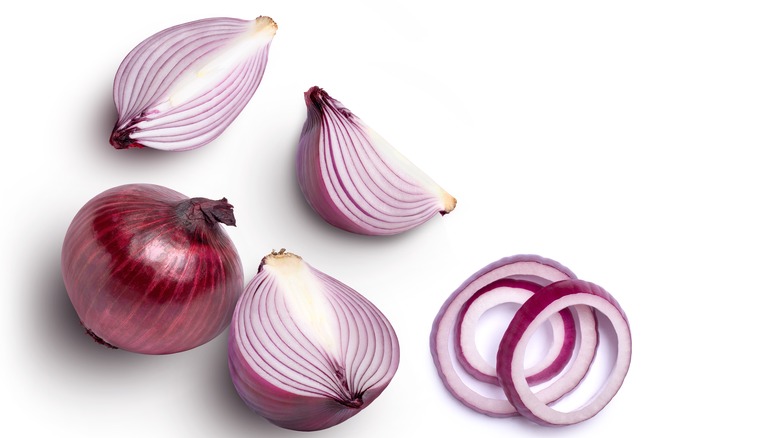 Several red onions, most cut lengthwise, with three crosswise-cut onion rings