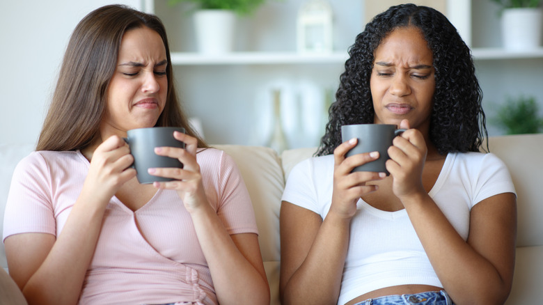 Two friends tasting disgusting coffee at home while sitting on a couch